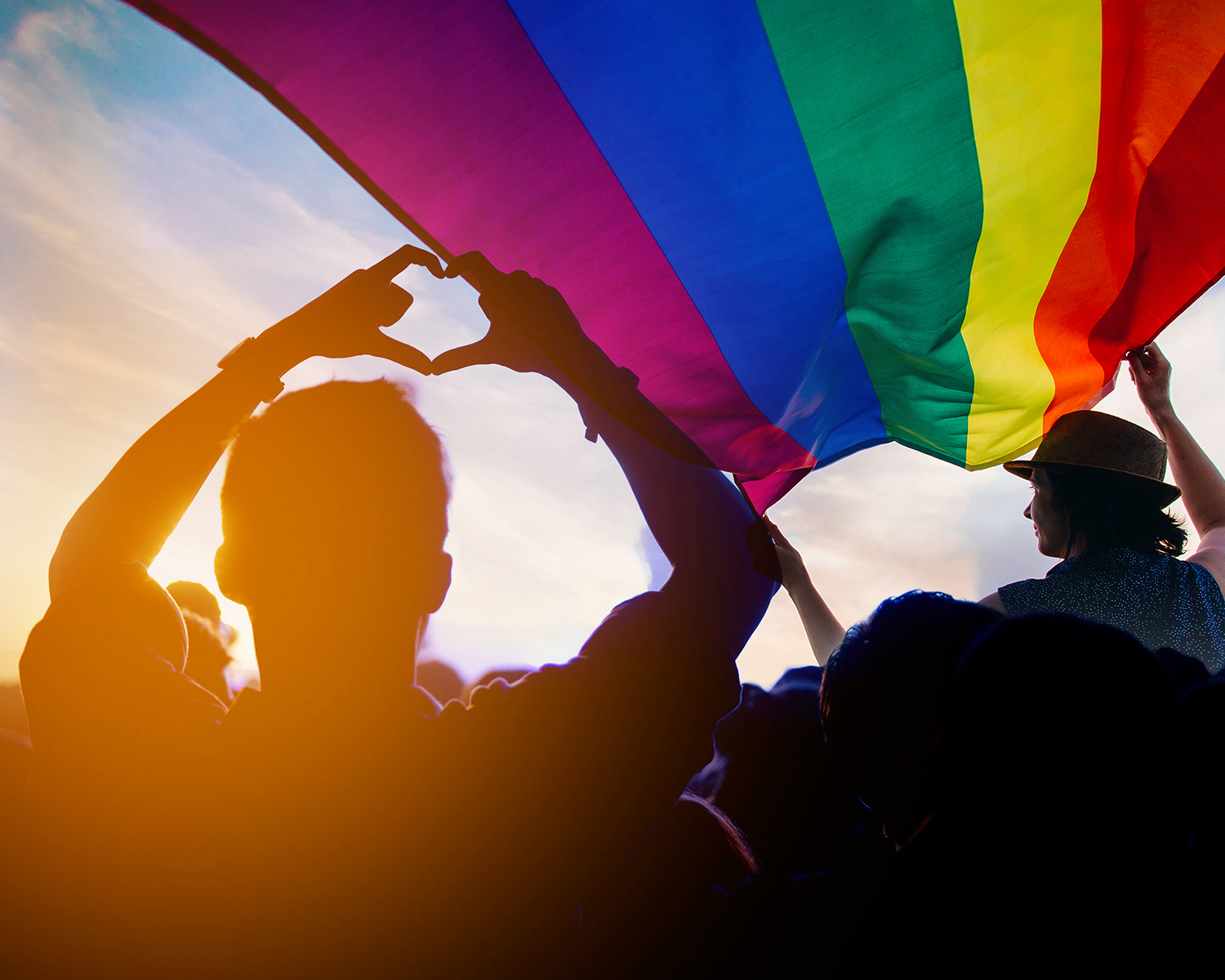 jemand zeigt Herzsymbol unter pride-flagge